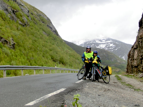 Jeg har syklet Kystriksveien tre ganger før, og hver gang har jeg tatt bilde akkurat her vi står nå. Det har aldri vært så mye snø på fjellet bak oss som det er i år. Alle vi møter forteller oss at de kan ikke huske å ha hatt en kaldere sommer enn det som har vært så langt i år.