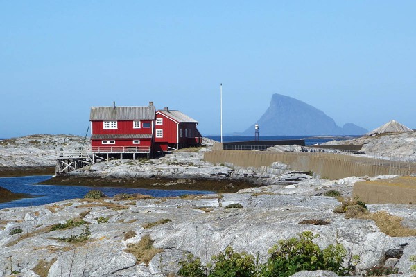 Sandsundvær med Lovund i bakgrunnen. Det litte trekantede taket til høye i bygningen er en brønn det det utrolig nok kommer opp ferskvann selv om vi er langt ute i havet og nærmeste ferskvannskilde er mange kilometer unna inne på fastlandet.