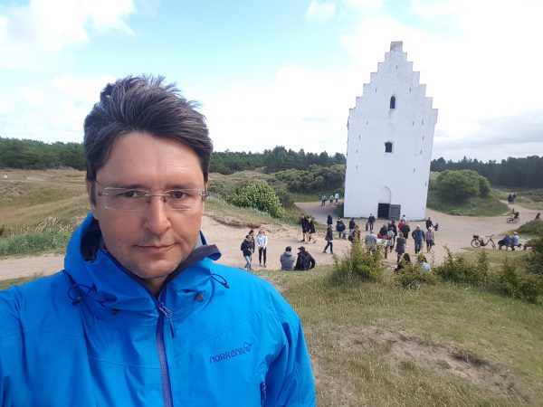 (12:00) Jeg tok en bitte liten avstikker for å se Den Tilsannede Kirke, og som dere ser bak meg var jeg ikke den eneste. Det gikk en jevn strøm med folk ut hit. Det er i det hele tatt litt i overkant mange turister i Skagen. Nok om det. Kirken ble bygd på 1300 tallet og etter en årelang kamp mot tilsanding ble den i 1795 overgitt til sanden. 